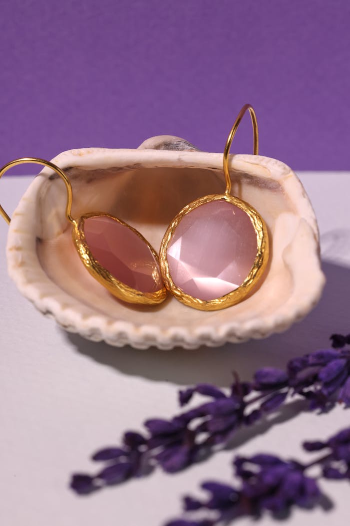 Close-up of gold-edged pink gemstone earrings in a seashell with lavender accents.